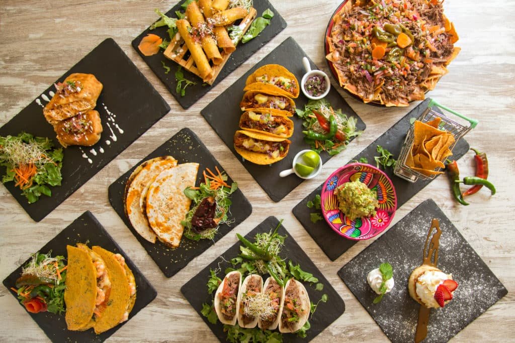 An overhead spread of tacos, quesadillas, taquitos, nachos, and guacamole