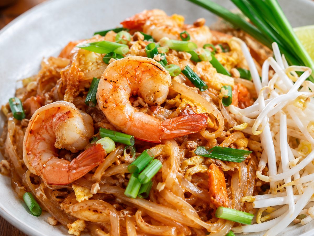 A plate of shrimp pad thai with bean sprouts and scallions